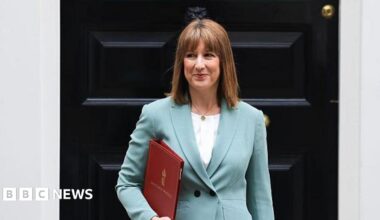 Rachel Reeves stands at the door of 11 Downing Street. She is wearing a mint green suit jacket and a white blouse. She is holding a red HM Government folder