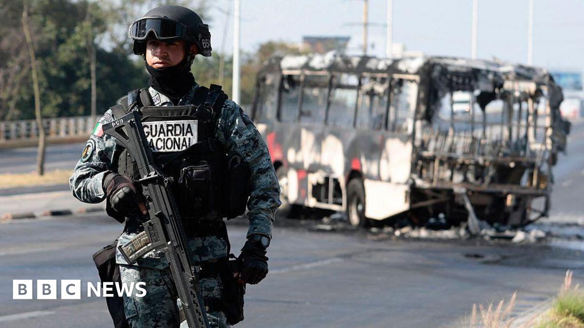 A National Guard member stands guard near a burnt bus set on fire by organised crime groups in response to an operation in Jalisco to arrest a high-priority security target, at one of the main avenues in Zapopan, state of Jalisco, Mexico, on February 22, 2026.