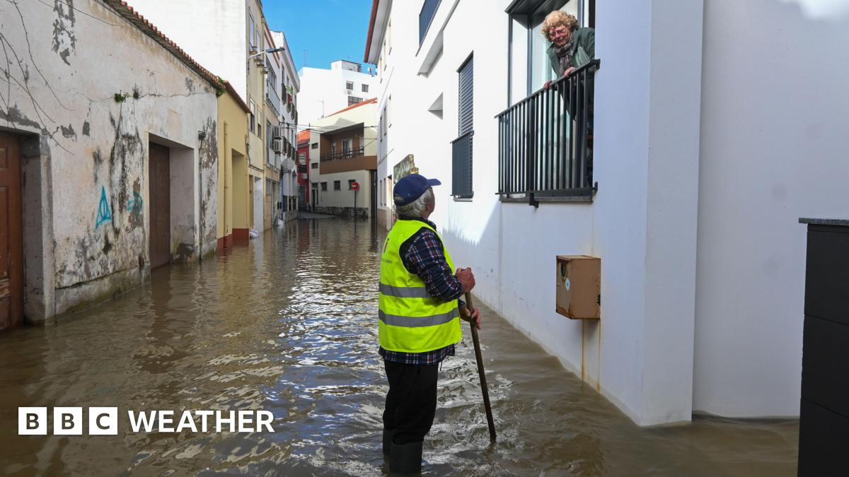 A woman looks down from a balcony on a man standing in a flooded street.