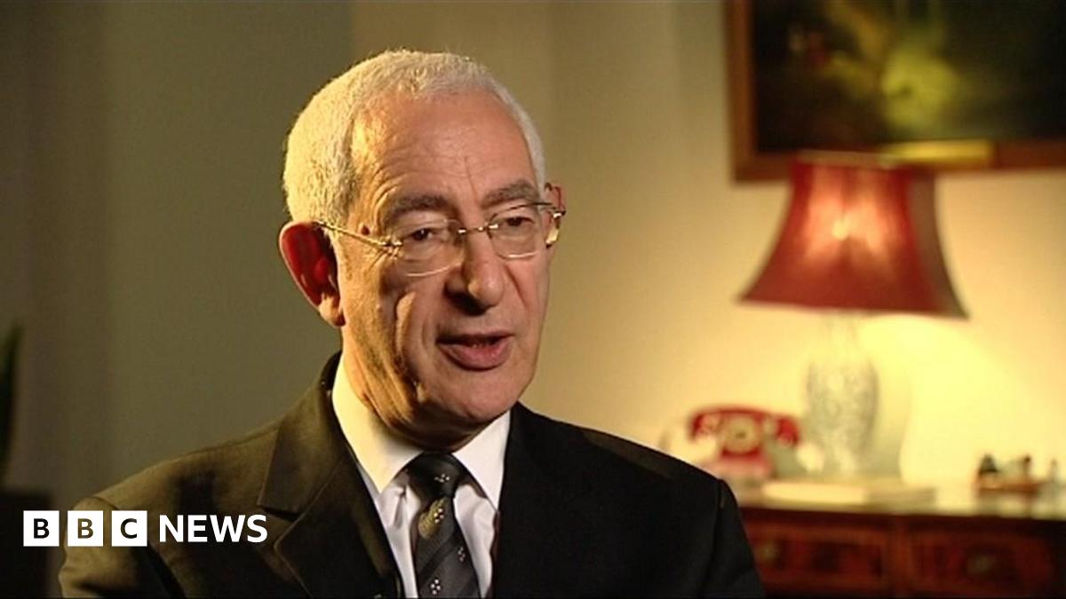 Lord David Triesman, wearing a black suit and speaking to the camera, in the dimmed light coming from a red lampshade