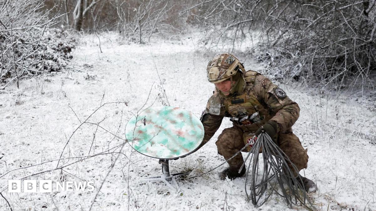 A soldier sets a Starlink dish down in a snowy field