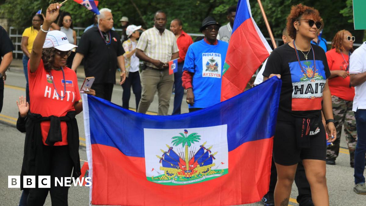 Marven, Rochelle and Guerline, pictured from behind, with their arms around each other looking out over a lake. Marwen is wearing a grey, collared T-shirt and is much taller than the two women.
