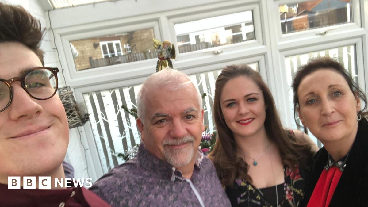 A road leading up to a roundabout, which has trees in the middle. A hotel is behind the roundabout.
