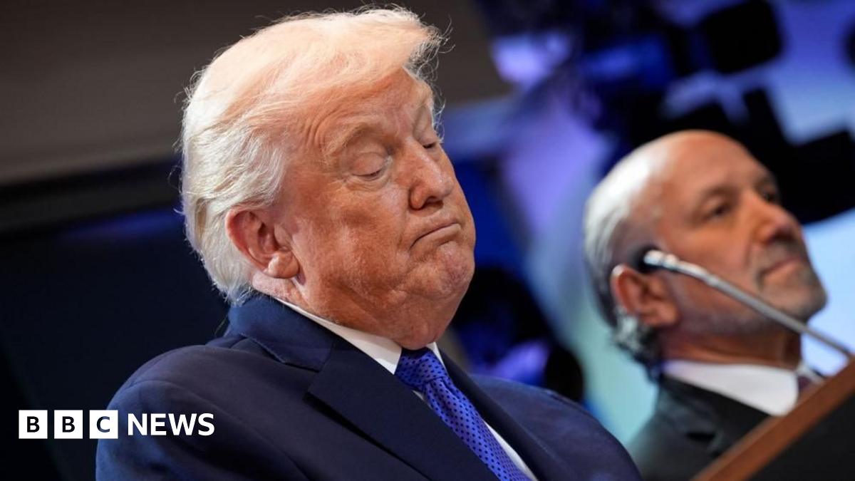Donald Trump looks down at his lectern, which is out of view. He is wearing a blue suit and a blue tie.