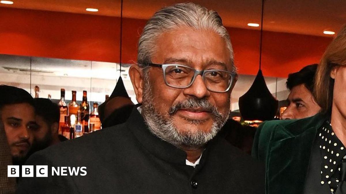 A middle-aged man with a short grey beard, wearing a high-necked suit jacket, looking at the camera.