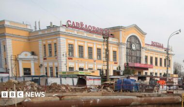 A yellow and white building with red lettering in Russian stands above construction works.