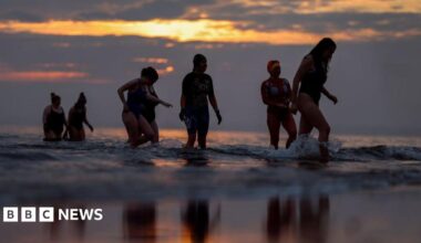 Seven women in swimming costumes wading pout of the sea at sunrise