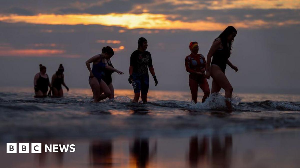Seven women in swimming costumes wading pout of the sea at sunrise