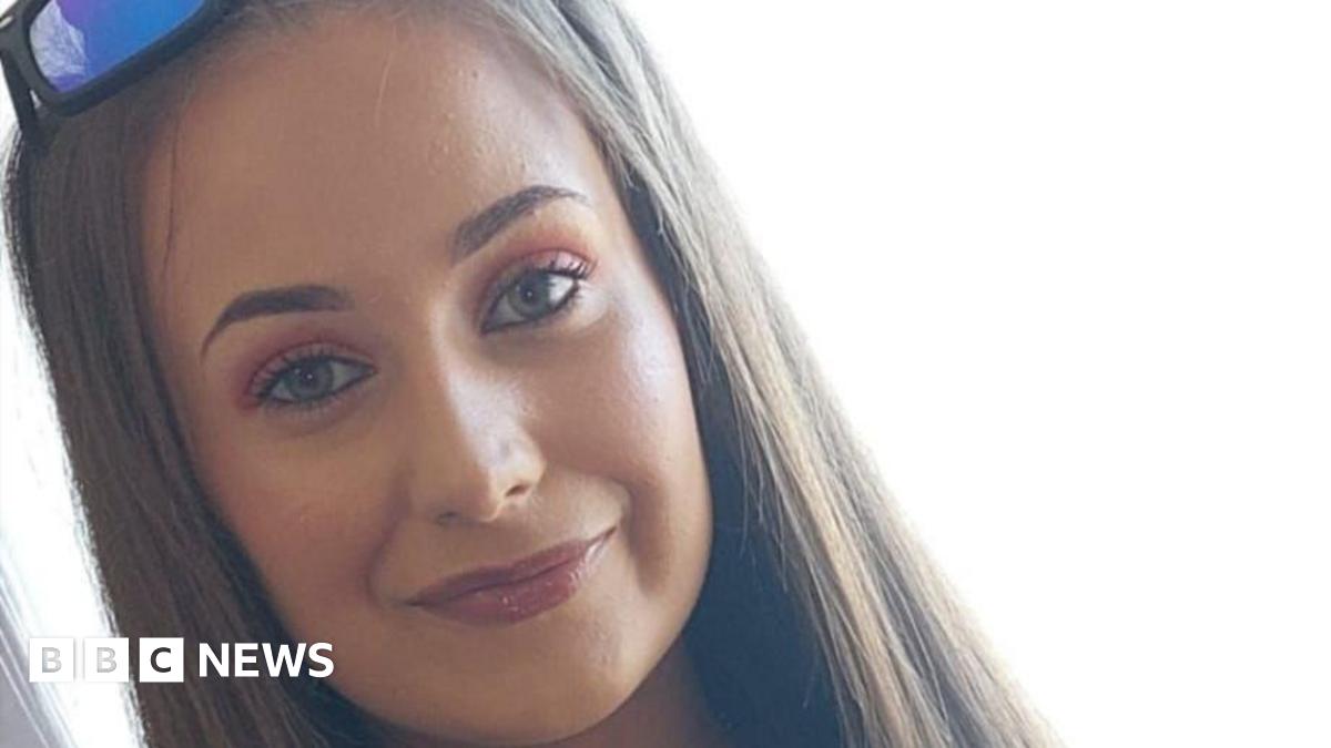 Chloe smiling at the camera. She has long straight light brown hair. She is wearing sunglasses on top of her head.