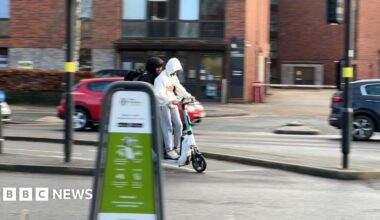 Transport Secretary Heidi Alexander smiles as she sits aboard a train carriage at a railway station. She is wearing a black dress and leopard print pashmina.