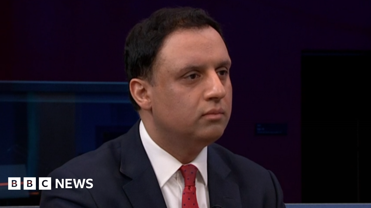 Anas Sarwar looks ahead with a serious expression on his face. He has short dark hair and wears a white shirt, red tie and black suit.