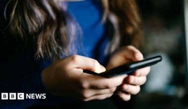A focused view of a young woman's hands holding a mobile phone indoors.