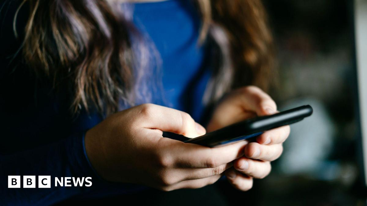 A focused view of a young woman's hands holding a mobile phone indoors.