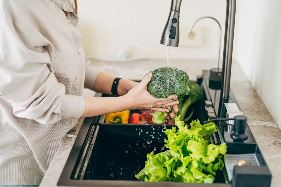 The hands of a person washing vegetables at the sink in the kitchen to prepare a fresh salad using tap water.