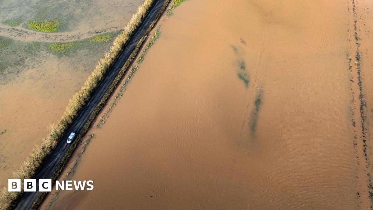 An aerial shot showing a car driving between flooded fields near the River Tone in Somerset.  The fields are almost completely invisible under brown floodwater