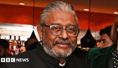 A middle-aged man with a short grey beard, wearing a high-necked suit jacket, looking at the camera.