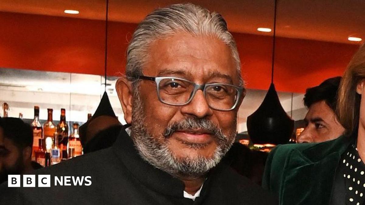 A middle-aged man with a short grey beard, wearing a high-necked suit jacket, looking at the camera.