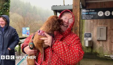 Wet looking woman in red coat holds dog