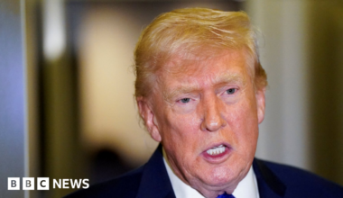 Headshot of US President Donald Trump, wearing a navy coat, white shirt and a royal blue tie