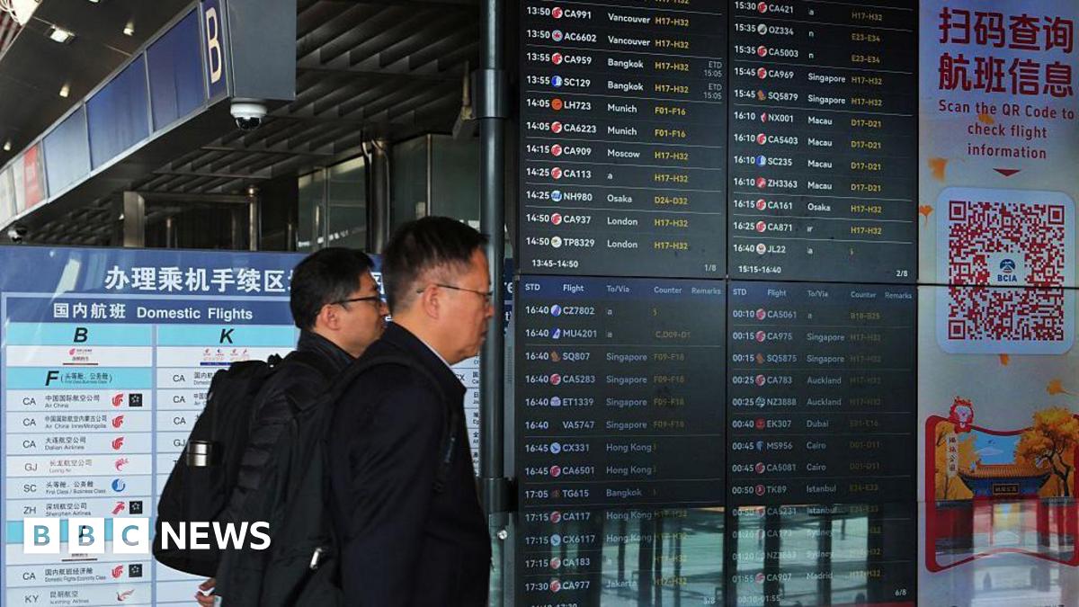 Two men walk past departures board at Beijing airport