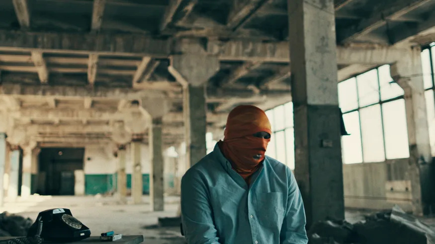 A former Russian army officer, who we have not named, sits in a warehouse in an orange balaclava.