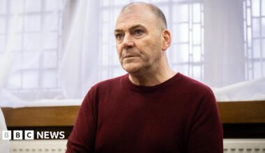 Mark Hehir wearing a burgundy jumper in front of a curtain