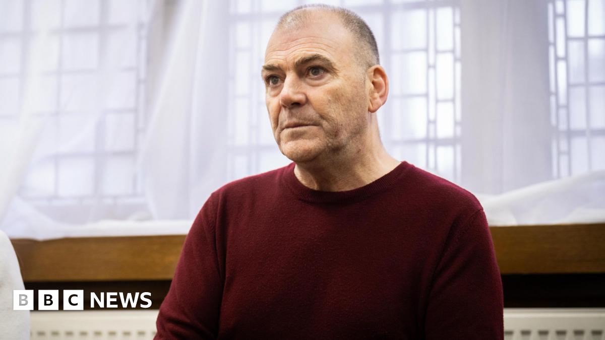 Mark Hehir wearing a burgundy jumper in front of a curtain