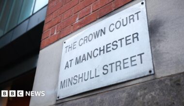 A metal sign botled to a concrete wall engraved with the words .The Crown Court at Manchester Minshull Street'.