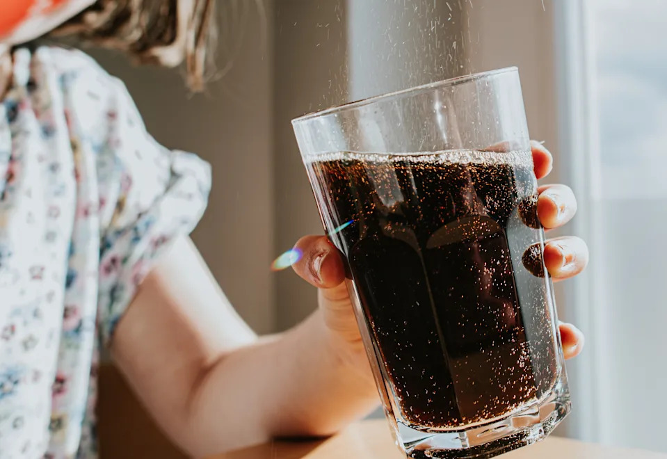 A child pours a fizzy cola drink into a glass.