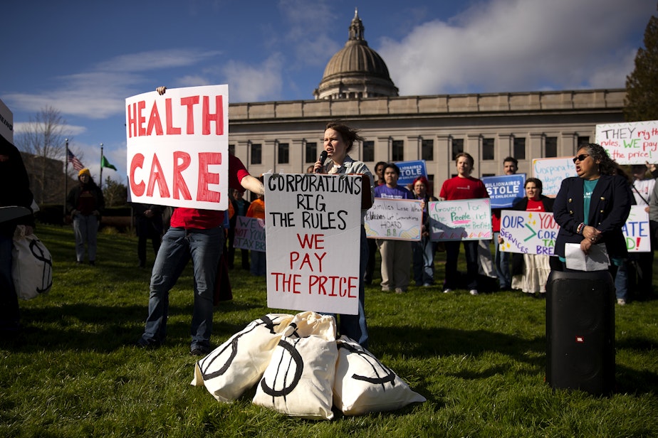 caption: Hannah Lindell-Smith, a volunteer with Washington Bus, speaks to a crowd during a “Corporations get tax breaks, working families pay the price” rally on Thursday, February 26, 2026, on the Washington State Capitol campus in Olympia. A coalition of workers, students, retirees and immigrants attended the rally.
