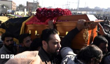 Several men carry a coffin through a huge crowd