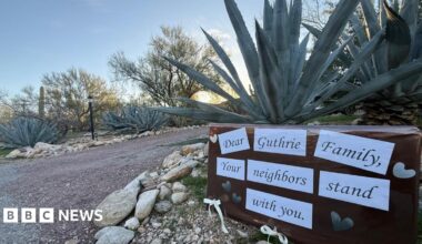 A signs stuck in front of a plant say "Dear Guthrie Family, your neighbours stand with you"