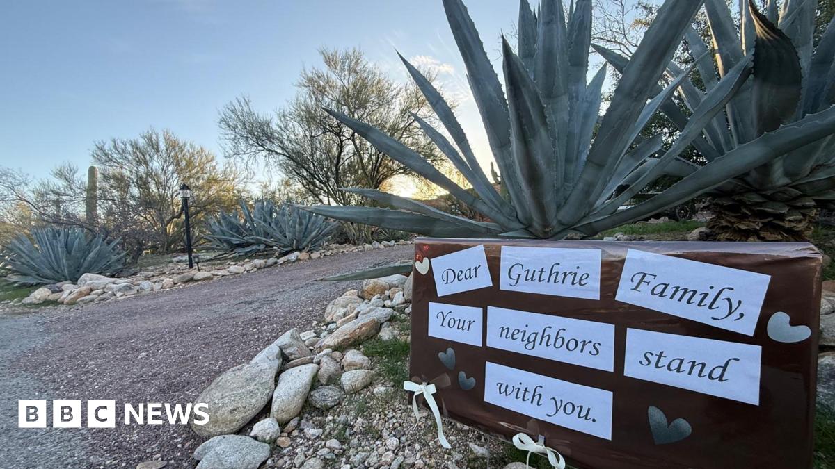 A signs stuck in front of a plant say "Dear Guthrie Family, your neighbours stand with you"