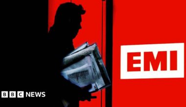A Silhouette of a man carrying a bundle of papers walking out of the door of the EMI record company in London. The EMI logo of three letters on a white background is surrounded in red.
