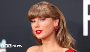 Taylor Swift, wearing a red dress, smiles for the camera during the Grammy Awards ceremony