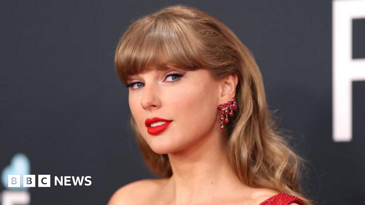 Taylor Swift, wearing a red dress, smiles for the camera during the Grammy Awards ceremony