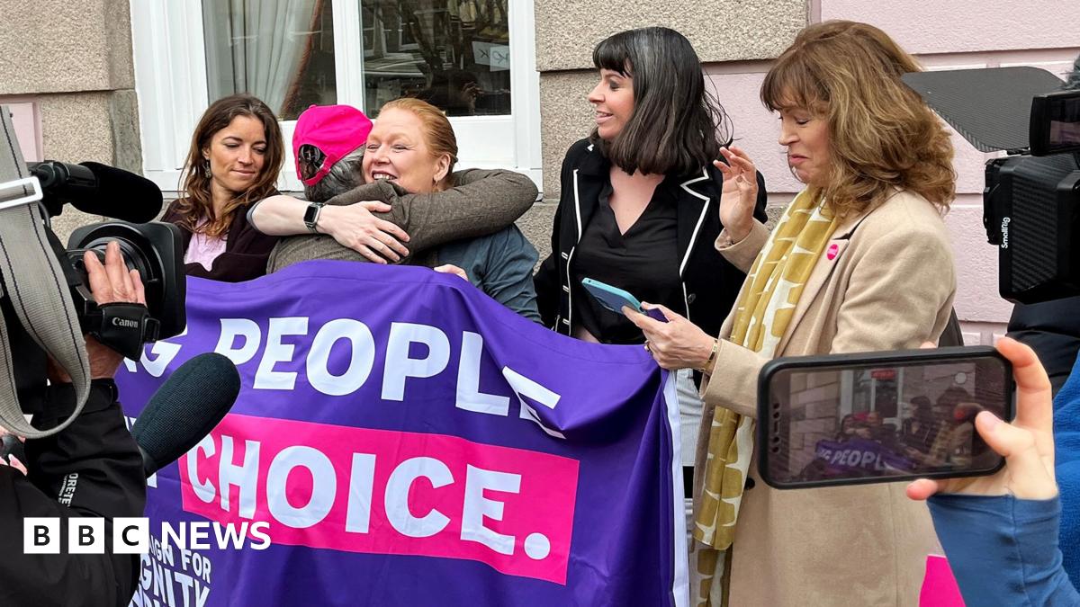 Five women celebrate with hugs next to a banner saying 'people, choice' with news cameras around them, outside on the street in Jersey on Thursday.