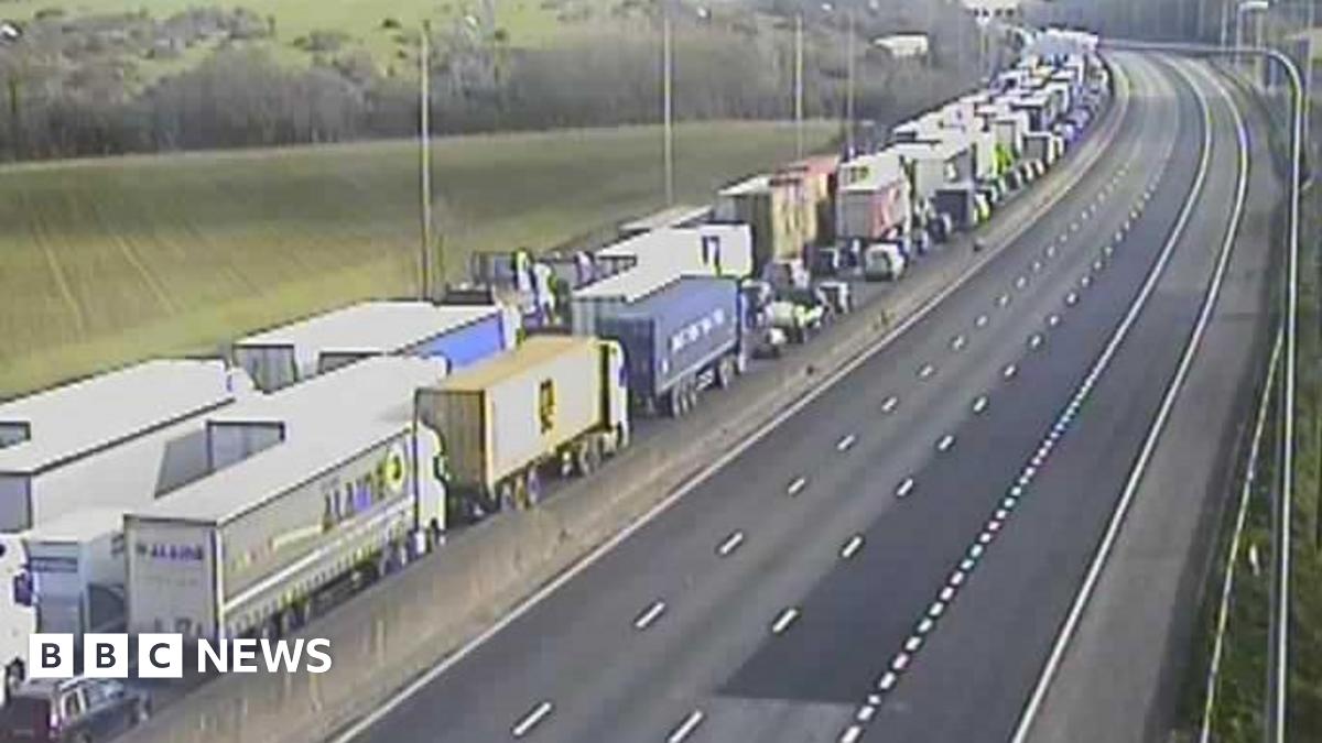 A queue of traffic made up of lorries and cars queueing on the M25. The other carriageway is completely empty.