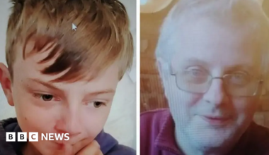 A young boy with blonde hair looking down and a blurred photo of a man with white hair and glasses