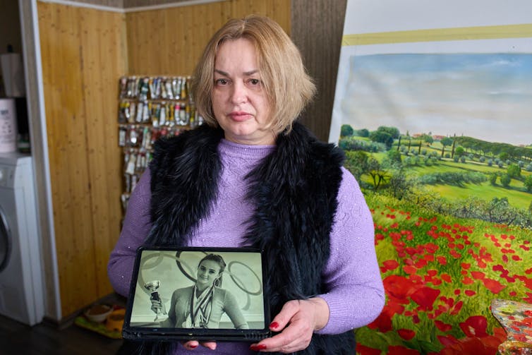A woman holds up a photo of a young woman draped in medals and holding a trophy