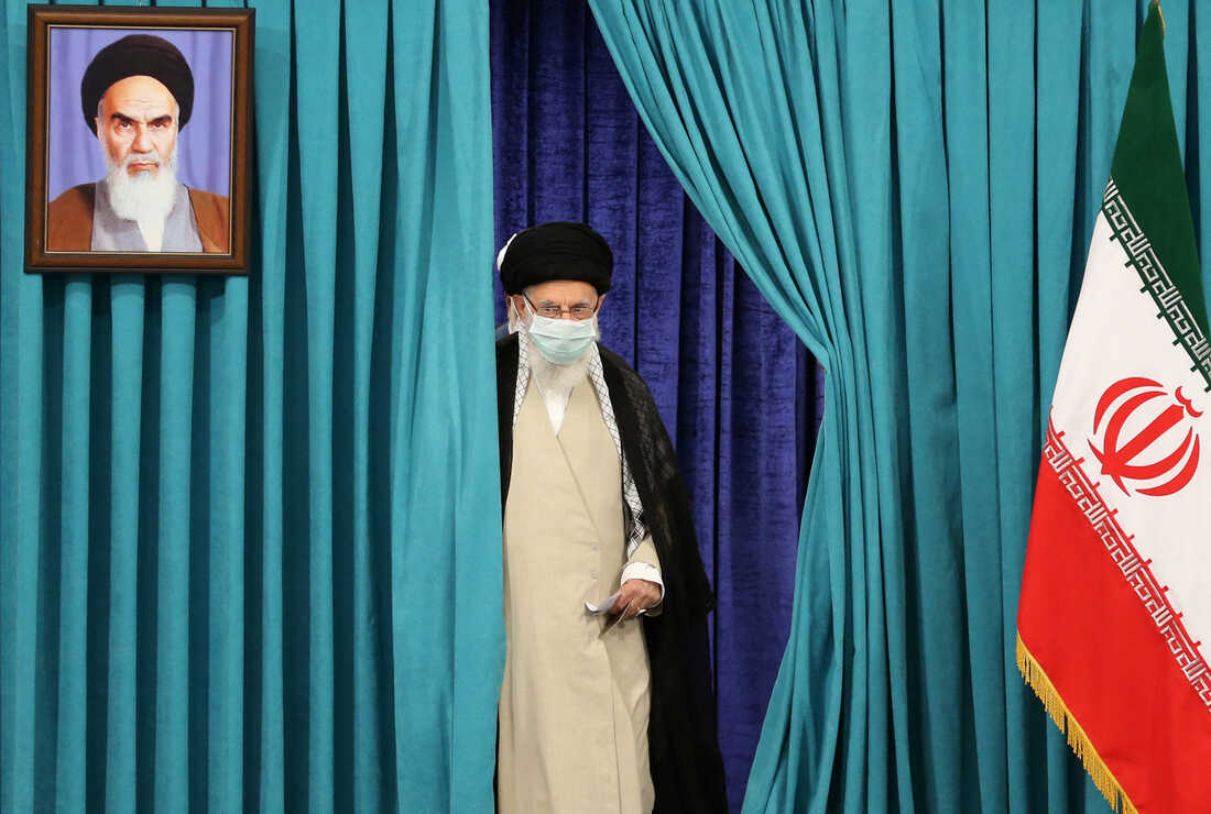 Emerging through a pair of teal curtains, Ali Khamenei wears a mask due to the COVID-19 pandemic as he arrives to cast his ballot during Iran's presidential election on June 18, 2021.