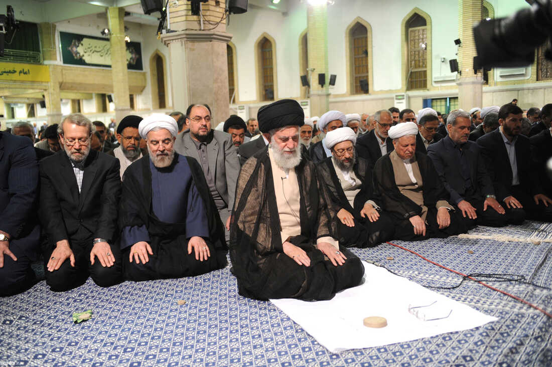 Kneeling on the floor, Iran's supreme leader, Ayatollah Ali Khamenei (center), prays with the Iranian president and other government officials, who are kneeling in rows behind him.