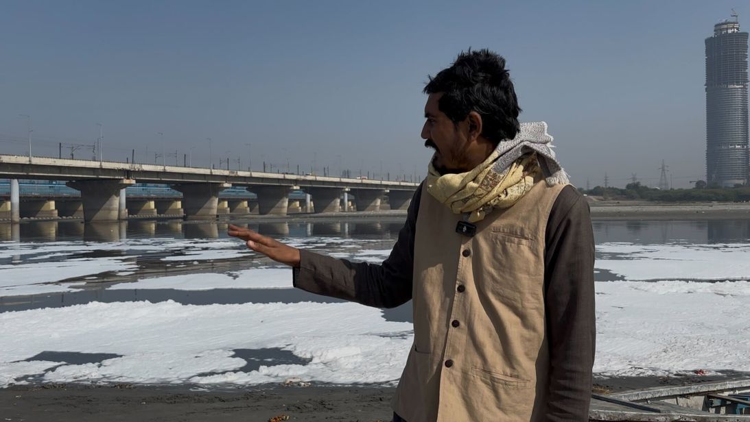 Pankaj Kumar on the banks of the Yamuna River, with toxic foam behind him.