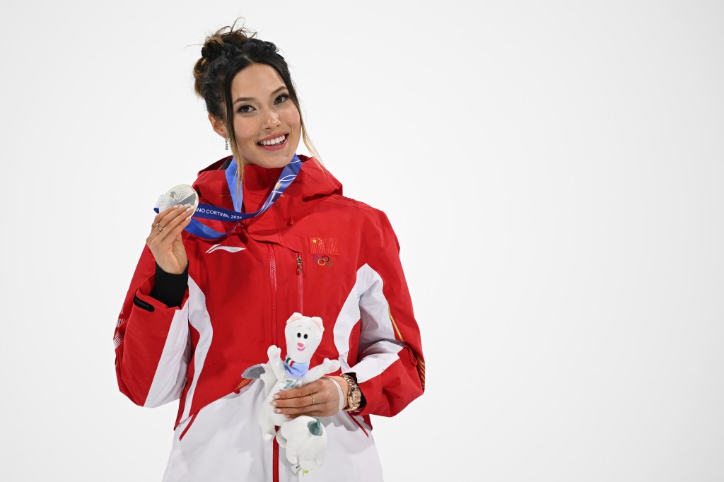 Ailing Eileen Gu posing with her silver medal and the Milano Cortina 2026 Winter Olympics mascot.