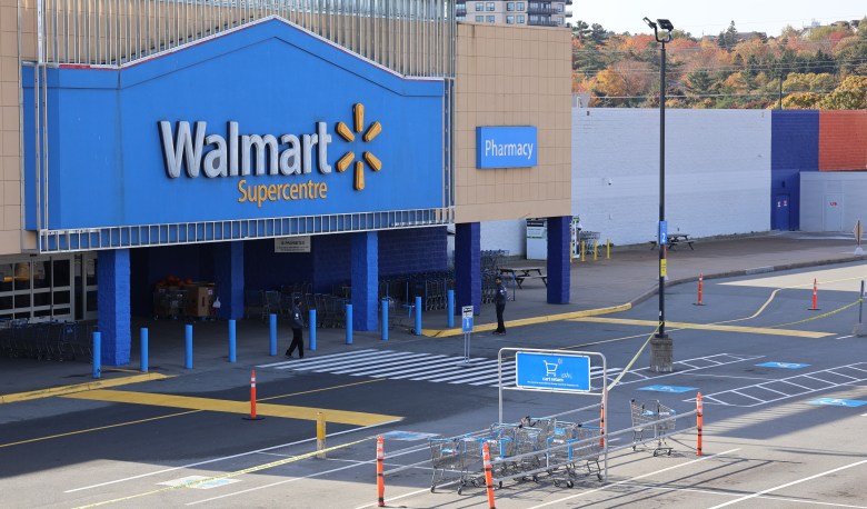 A security guard walks around in front of the main entrance of a Walmart store. The parking lot is empty and the carts are in the corral.