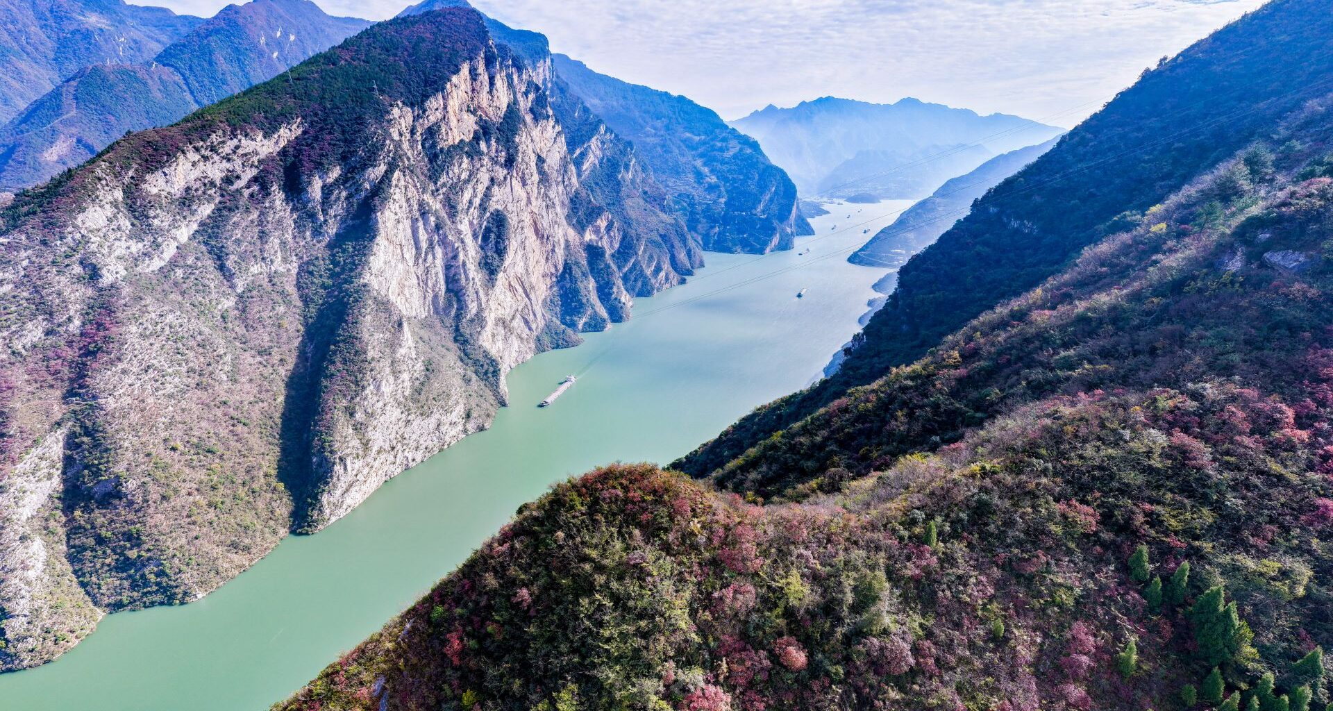An aerial shot of the Yangtze river, a teal colored strip of water seen between two lush, rocky peaks.