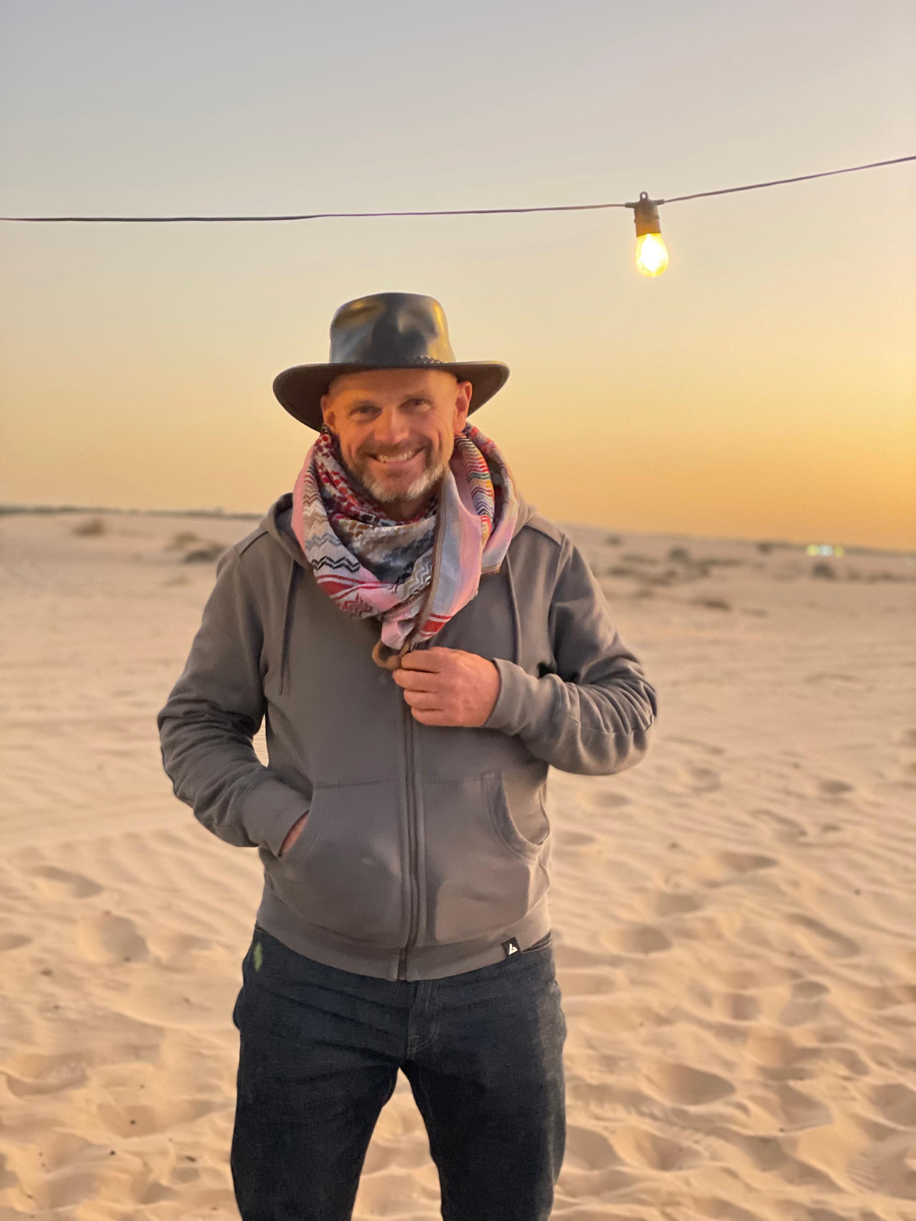 Jonty Summers in Dubai for T2, standing on a sandy desert at sunset with a string of lights overhead.