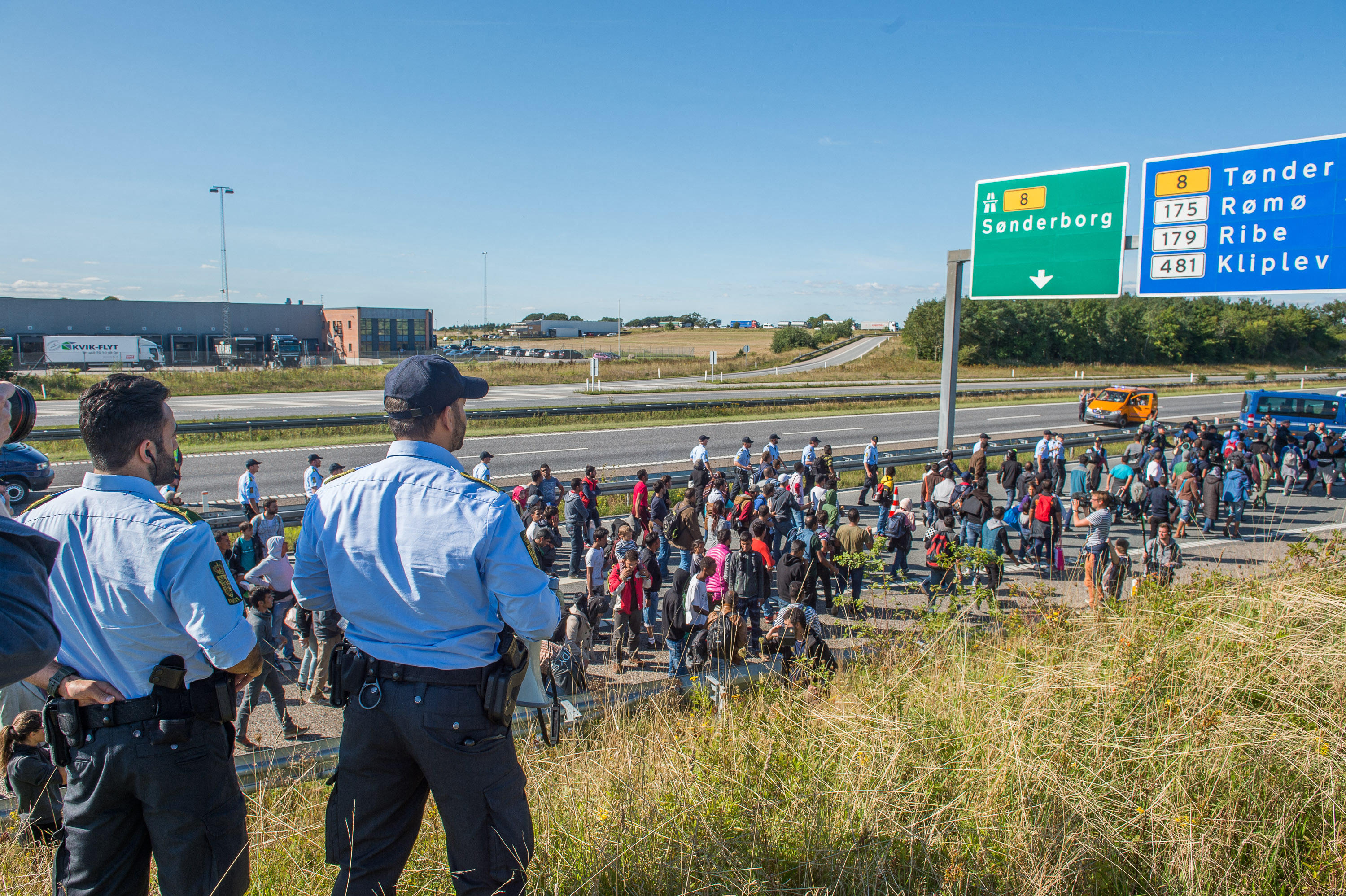 Police officers overseeing refugees walking along a Danish motorway.