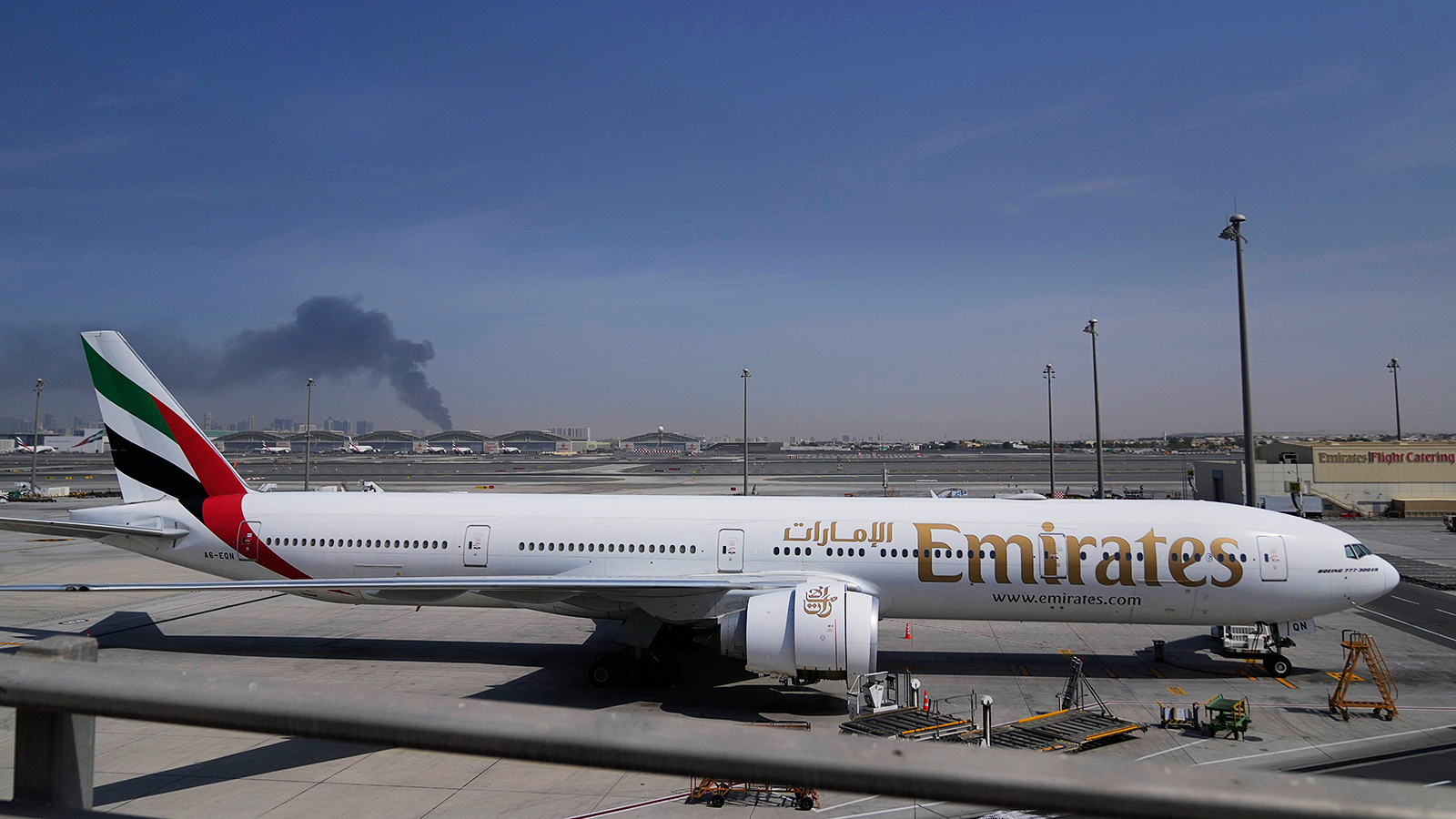 Emirates plane at Dubai International Airport with smoke from an Iranian strike visible in the background.
