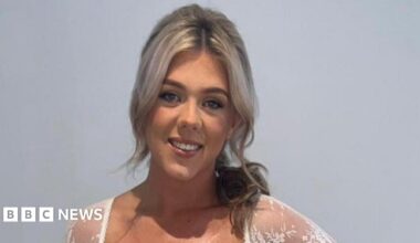 Amy Doherty who has light blonde hair partly pulled back over her left shoulder, she is wearing a white lace top and smiling at the camera.